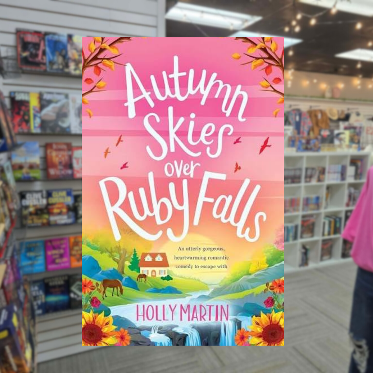 Autumn Skies over Ruby Falls by Holly Martin paperback cover featuring pink autumn skies, colorful fall leaves, a countryside cottage, horses, and a waterfall.
