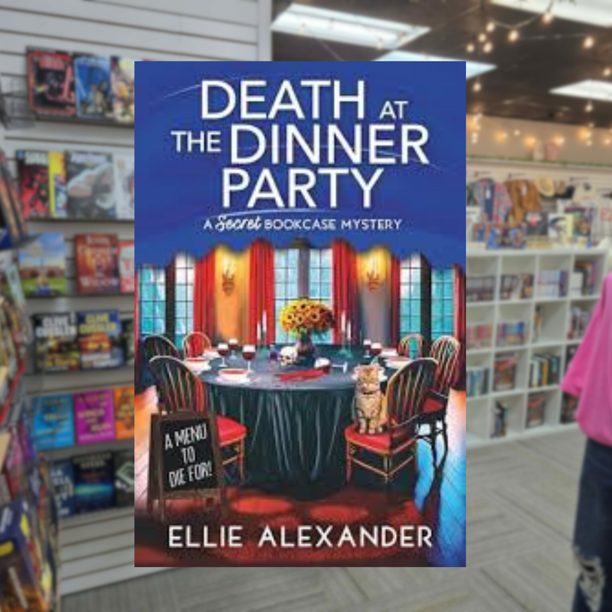 Death at the Dinner Party by Ellie Alexander cozy mystery paperback cover featuring an elegant dining room with a beautifully set table, red curtains, and a mysterious atmosphere.