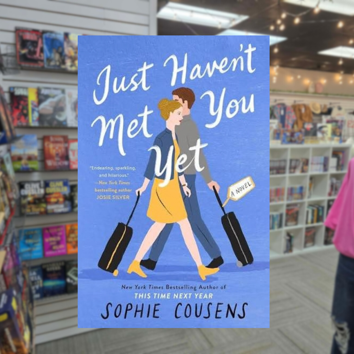 Just Haven't Met You Yet by Sophie Cousens paperback romantic comedy book cover featuring an illustrated couple walking with suitcases against a blue background
