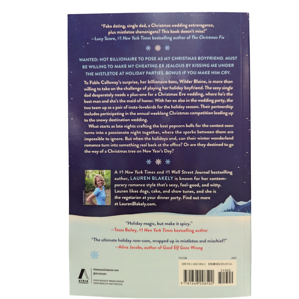 My Favorite Holidate by Lauren Blakely Christmas romance paperback cover featuring a couple embracing in a snowy mountain setting beside a festive red cabin, with snowflakes against a dark blue sky.