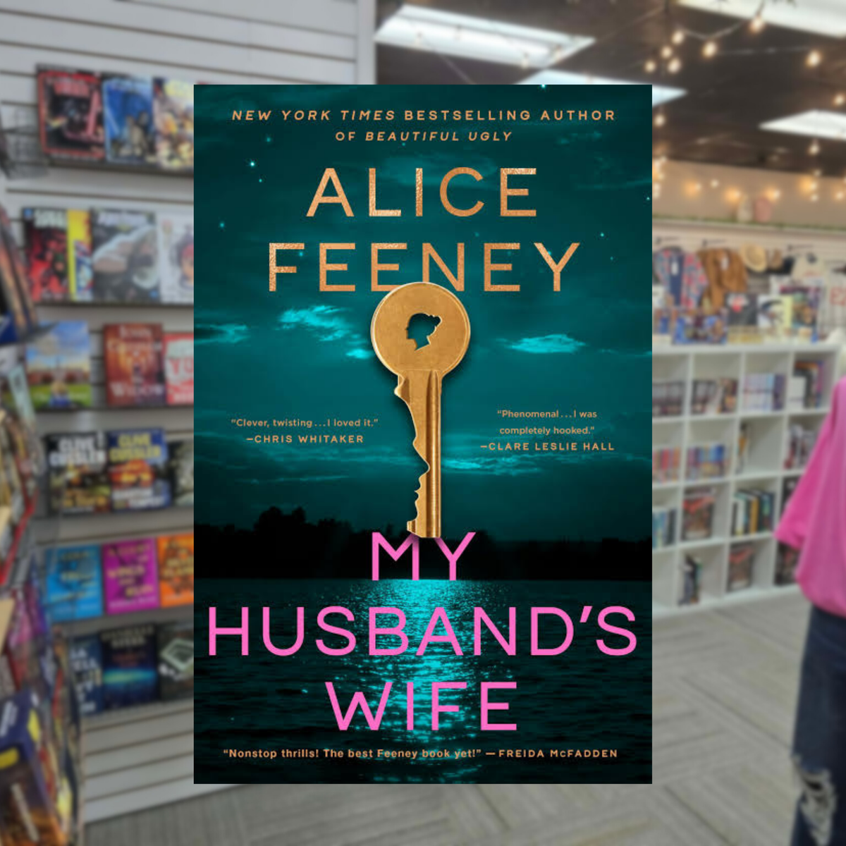 My Husband's Wife by Alice Feeney psychological thriller book cover featuring a large gold key with a woman's silhouette in the keyhole, a dark teal sky, water, and bold pink lettering.