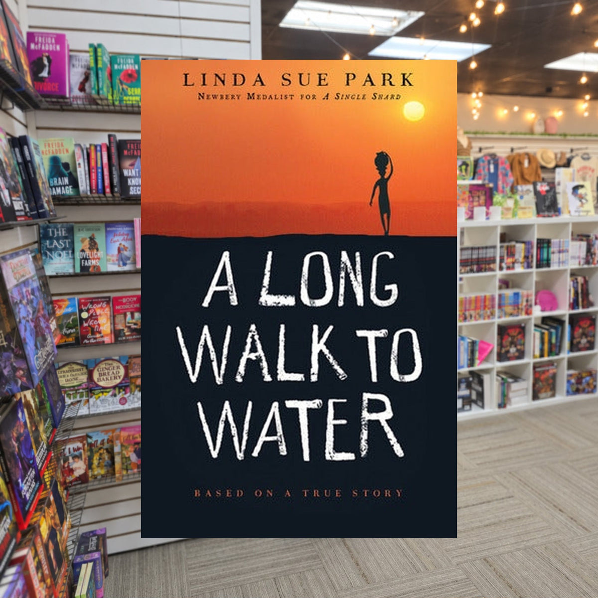 A Long Walk to Water: Based on a True Story by Linda Sue Park — actual cover on The Perk bookstore background