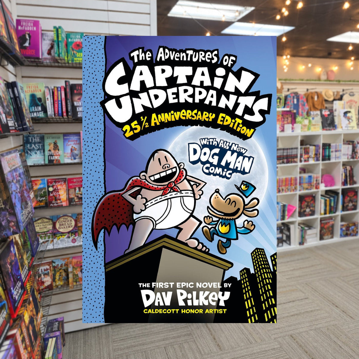 The Adventures of Captain Underpants (Now With a Dog Man Comic!): 25 1/2 Anniversary Edition by Dav Pilkey — actual cover on The Perk bookstore background