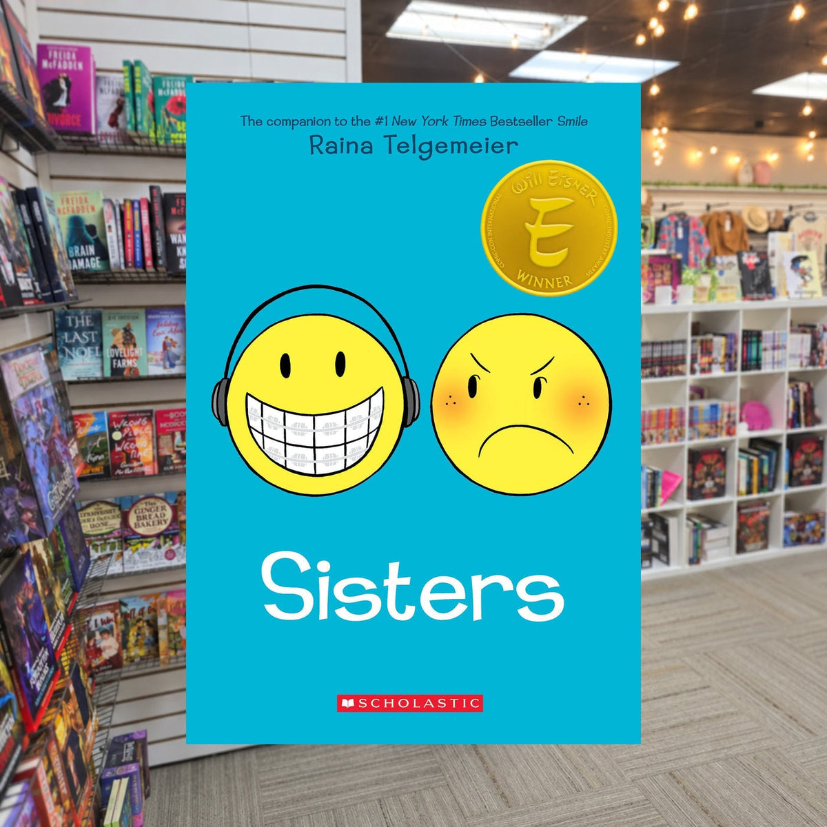 Sisters: A Graphic Novel by Raina Telgemeier — actual cover on The Perk bookstore background
