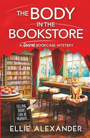 The Body in the Bookstore by Ellie Alexander cozy mystery paperback cover featuring a charming bookstore interior with bookshelves, a reading table, large windows, and red curtains.