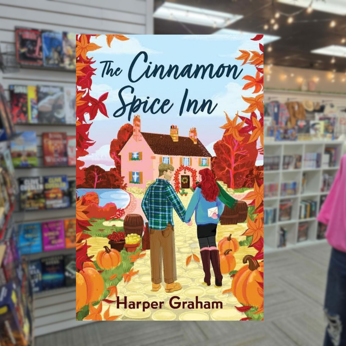 The Cinnamon Spice Inn by Harper Graham paperback cozy autumn romance book cover featuring a couple outside a charming inn surrounded by fall leaves and pumpkins