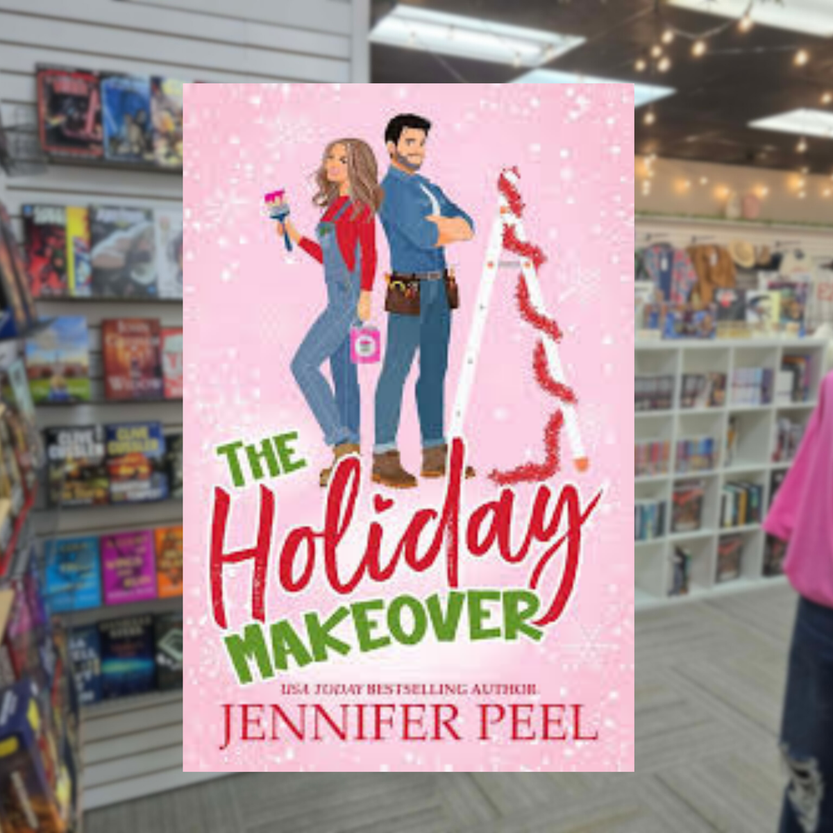The Holiday Makeover by Jennifer Peel Christmas romance book cover featuring a pink snowy background, an illustrated blonde woman holding a paint roller, a dark-haired man, and a decorated Christmas tree.