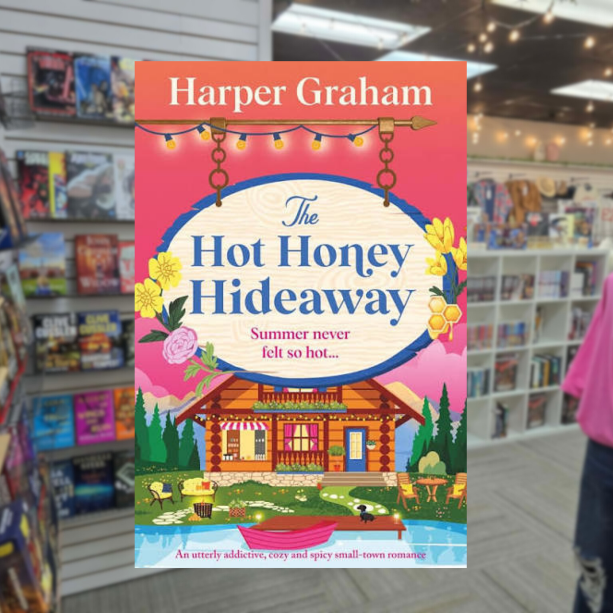 The Hot Honey Hideaway by Harper Graham spicy small-town romance paperback cover featuring a cozy lakeside log cabin café, colorful flowers, honeycomb details, string lights, and a vibrant pink and orange summer sunset.